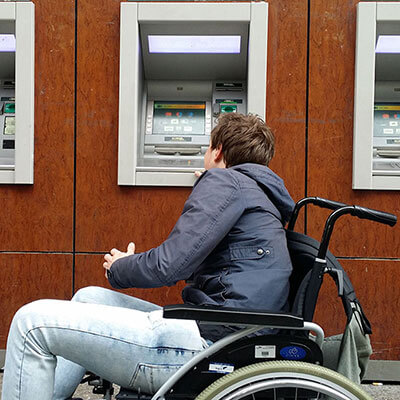 Foto van een man in een rolstoel welke niet bij een pinautomaat kan