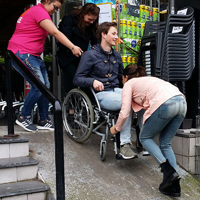 Een foto waarbij een rolstoel een winkel entree met een helling van 45 graden wordt opgeduwd